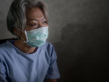 mature woman with grey hair in hospital patient gown and mask infected by COVID-19