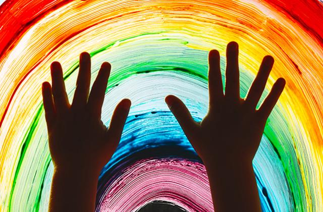 Child hands touch painting rainbow on window.
