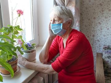 Old woman with a facemask looking out a window