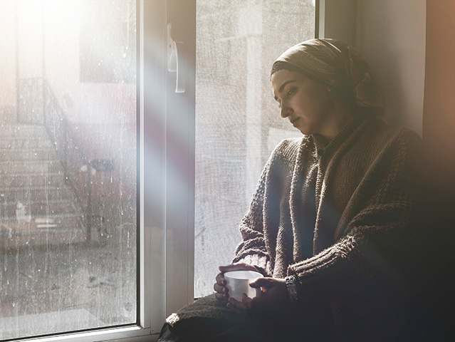 Young Muslim woman sits on window sill and looking away. 