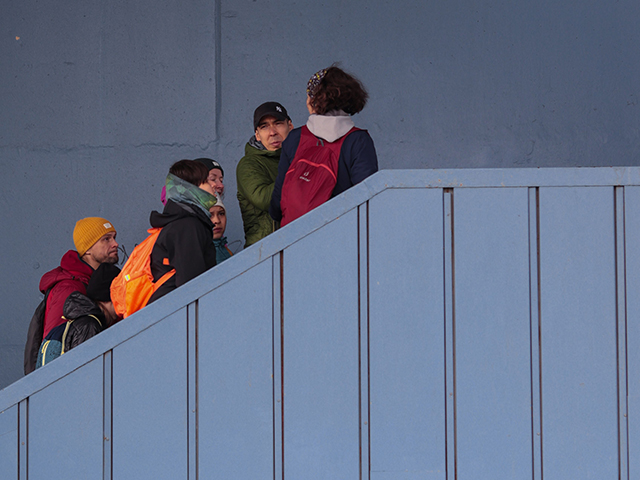 A diverse group of friends walking up a blue staircase with colorful backpacks.