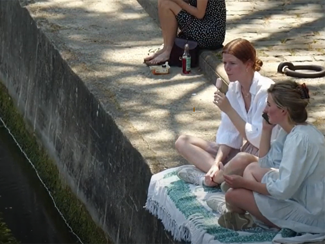Two young women sitting next to a canal.