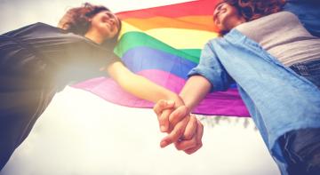 Two women holding hands against the backdrop of the rainbow flag.