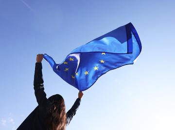 Woman holding European Union flag against blue sky 
