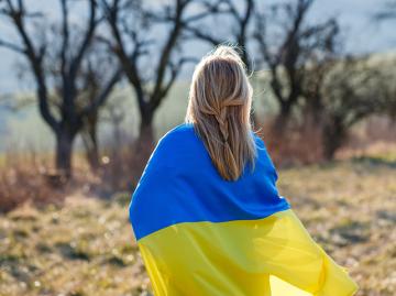 Woman covered by ukrainian flag standing in field.