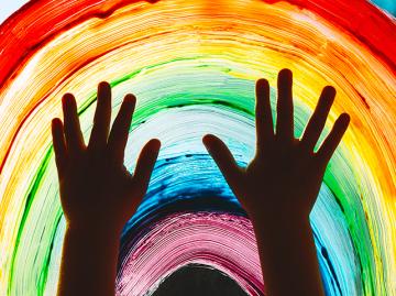 Child hands touch painting rainbow on window.