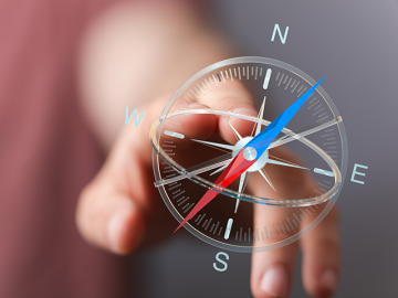 Close-up of a hand pointing to a compass