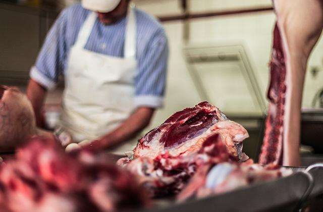 Butcher cutting raw meat with a knife at table in the slaughterhouse