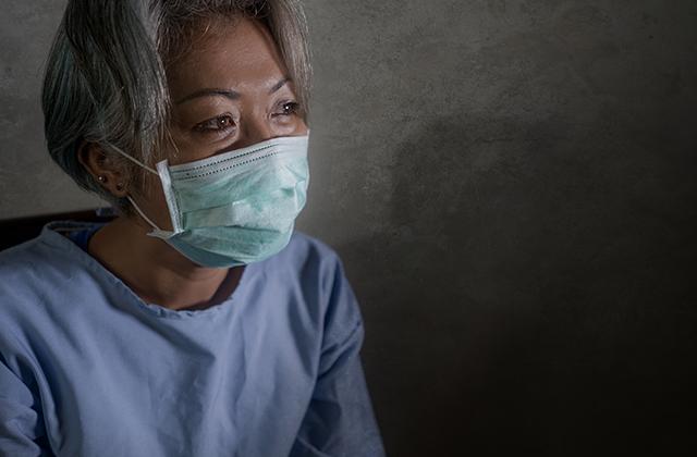 mature woman with grey hair in hospital patient gown and mask infected by COVID-19