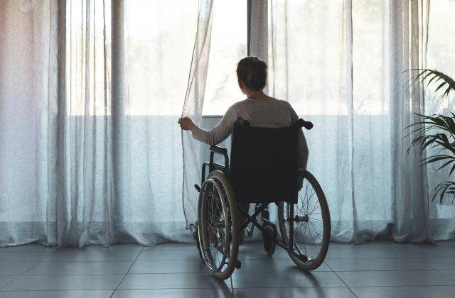 Woman in wheelchair all alone looking out the window as if she was waiting for someone