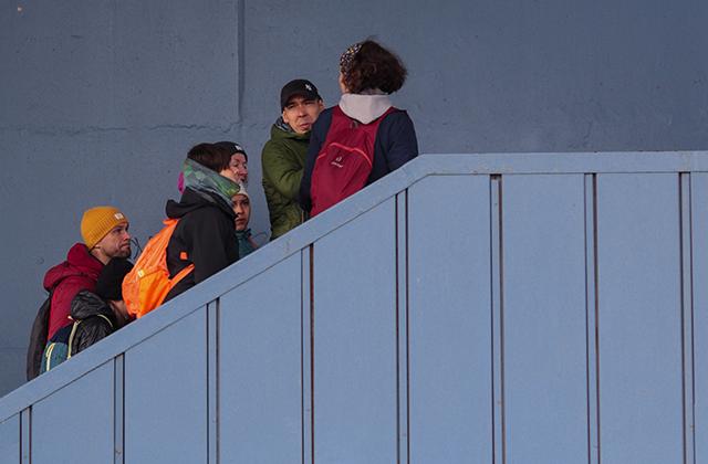 A diverse group of friends walking up a blue staircase with colorful backpacks.