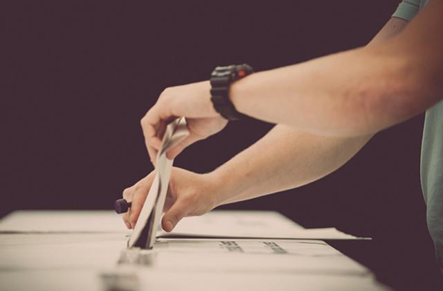 Hands placing a vote into a ballot box.