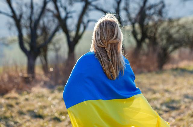Woman covered by ukrainian flag standing in field.