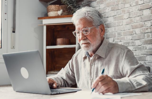 Concentrated senior male in glasses work on laptop from home office read email electronic document. 