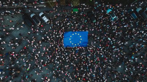 Blue and yellow E U flag surrounded by pedestrians in dark clothing